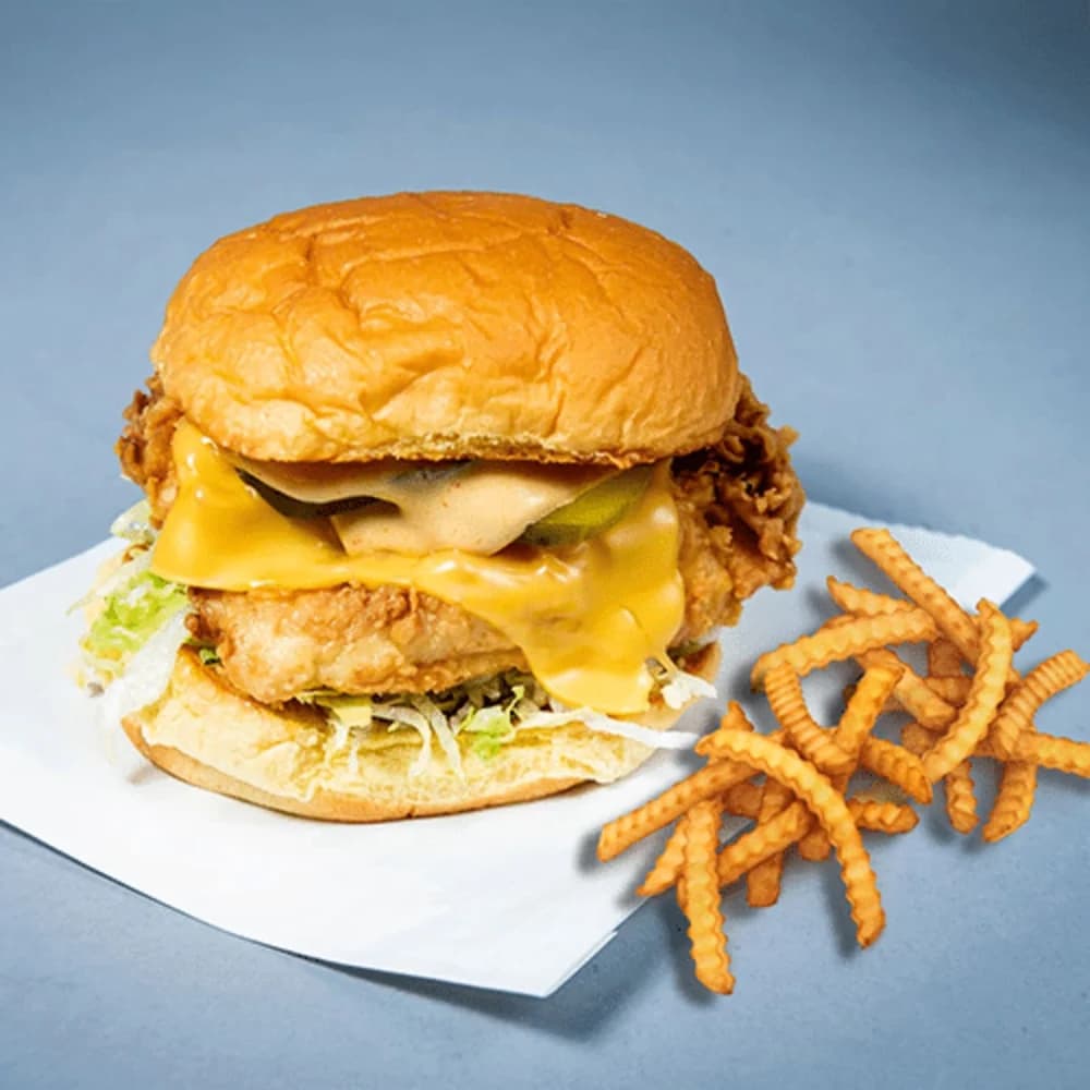 Crispy fried chicken op een potato bun, met American cheese, sla, augurk, ui, tomaat en smash saus. Krokant tot de laatste hap.