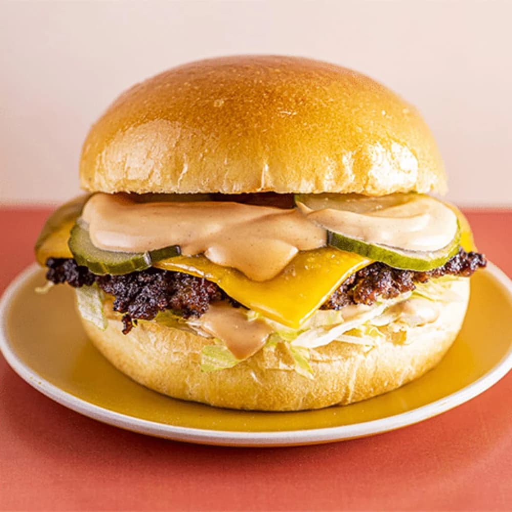 Zachte brioche, gesmashte Angus beef, American cheese, sla, augurk, ui, tomaat en smash saus. Zelfde smash, zachtere bite.