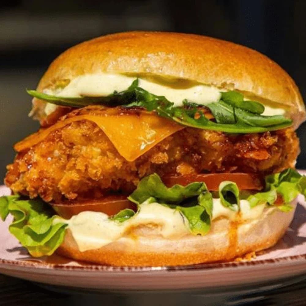 Crispy chicken met cheese, sla, augurk, ui, tomaat en smash saus op brioche. Krokant tegen zacht, elke hap opnieuw.